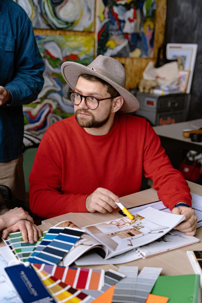 A thoughtful designer in a red sweater reviews color swatches for a project in a vibrant workshop setting.